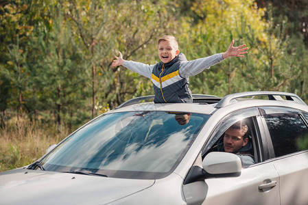 快乐的小男孩张开双臂站在开着的汽车天窗上而父亲图片