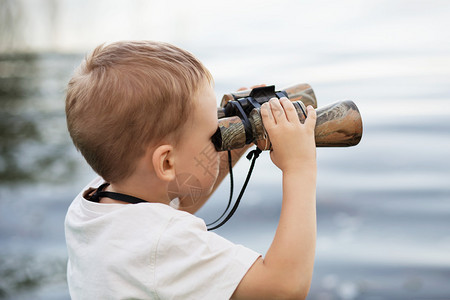 通过双筒望远镜在河岸上看的小男孩的画像可爱的孩子在水或池塘前图片