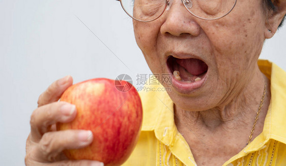一位戴着眼镜没有牙齿的老妇人试图吃红苹果牙科健康问题概念老年患者图片