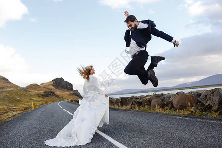 新娘笑着走在高速公路上与新郎跳跃的新娘在蜜月时图片