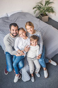 快乐的父母和孩子们在家里一起坐在床上的高角度视野图片