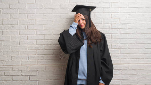 穿着研究生制服站在白砖墙上站着的年轻黑发女人头顶用手压住图片