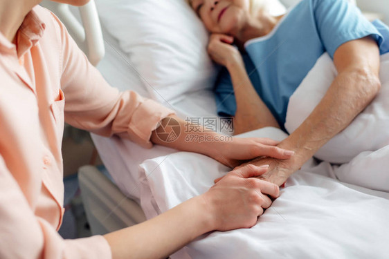 女儿坐在年长母亲身边躺在床上和在医院握图片