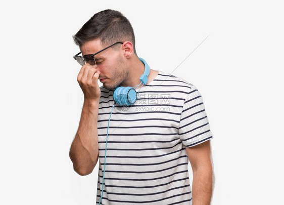 穿着耳机的英俊青年男子在擦鼻子和眼睛时感到疲劳和头痛压力图片