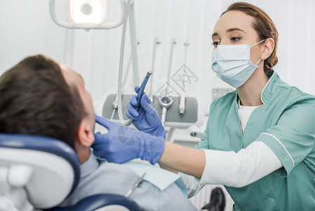 戴口罩的女牙医手持牙科仪器并触摸牙科诊图片