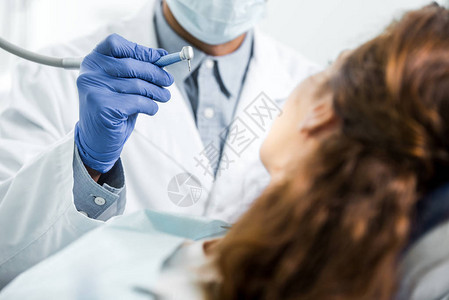 白色大衣牙医在女病人附近持有牙科工具的切图片