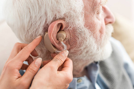 女帮助灰色头发男子佩戴助听器的妇图片