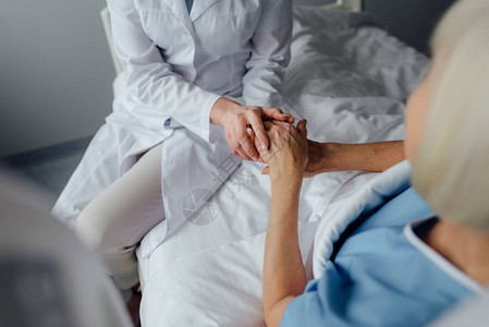 与在医院床上躺着的高级妇女握手的女医图片