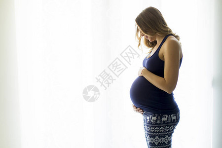 漂亮的年轻孕妇站在房间的窗边背景图片