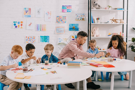 教师和跨种族儿童在课堂的桌子上一起绘画图片