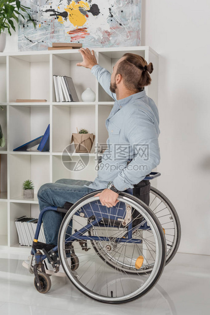 坐在轮椅上的残疾人试图伸手去拿书架上的书图片