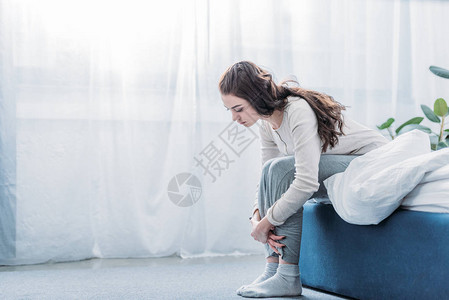 愤怒的女人抱着膝盖坐在家里的床上图片