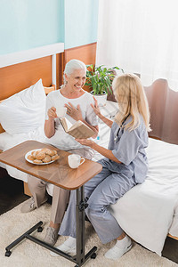 在医院里微笑的年长妇女和护士阅读书和喝茶的高图片