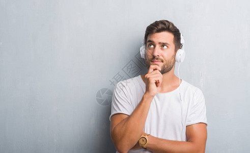 灰色格朗基墙上的帅哥戴着耳机听音乐严肃的脸思考问题图片