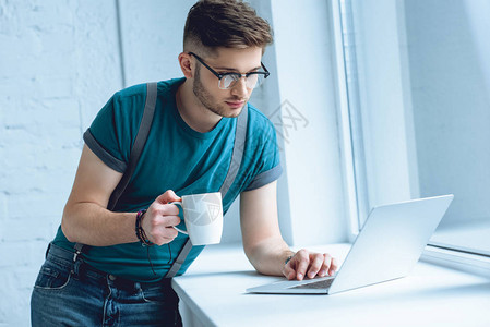 戴眼镜的青年男子拿着咖啡在窗台上图片