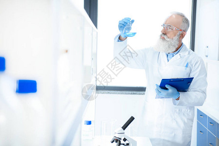 在化学实验室内持有含试剂和剪贴板的酒瓶的高级图片