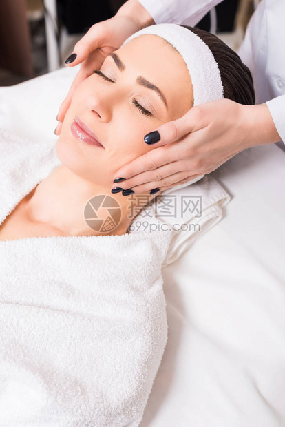 美容师给睡在浴袍和美容院的发带上的女人手工图片