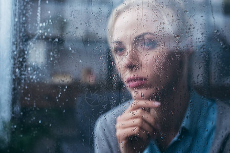 深思痛心的成年妇女用雨滴通过窗口在图片