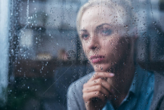 深思痛心的成年妇女用雨滴通过窗口在图片