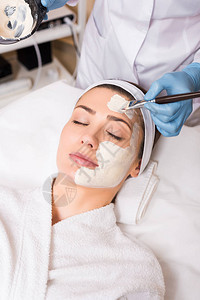 美容师用化妆刷在女脸上涂抹化妆面膜并在美图片