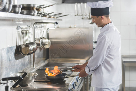 英俊厨师在餐厅厨房用火煎牛排的侧视图图片