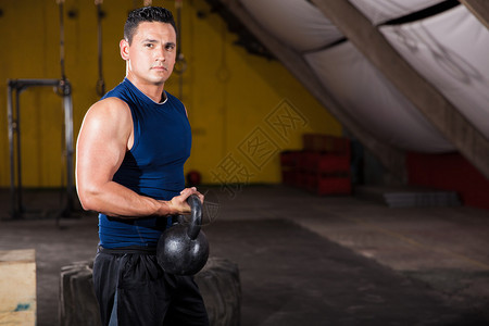 强健的年轻人举起一个木铃作为他在交接健身房图片