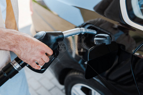 持有燃料泵和加油站为黑色汽车加油的男图片