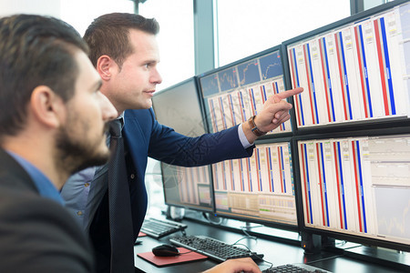 买卖股票的商人股票交易员在多个电脑屏幕上查看图表指数和字同事们在交易员办公室讨论图片