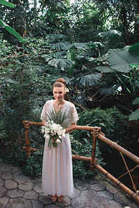 年轻新娘穿着白衣服在热带花园中用背景图片
