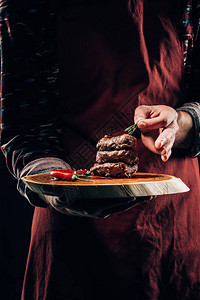 围裙主厨中弹手持木板配有美味的烤肉图片