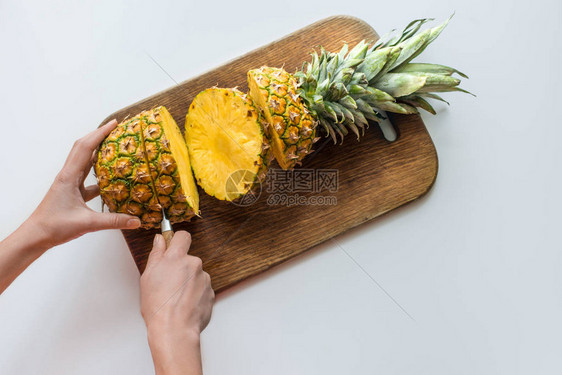 在木板上切新鲜菠萝的人顶视图与白色隔离图片