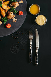用刀子和美味的烤土豆鸡翅和酱汁在黑色上图片