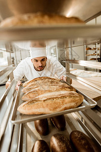 英俊的面包师在烘烤制造时把新鲜面包图片