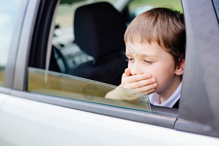 坐在儿童安全座椅上的汽车后座上的7岁小孩用手捂住嘴患有晕车图片