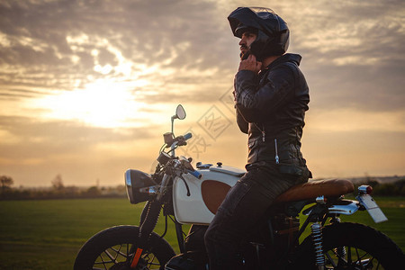 在日落时坐在摩托车上戴头盔的自行图片