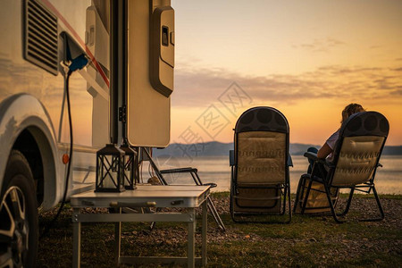 风景秀丽的房车露营地露营车在休闲车公园女人在椅子上放松背景图片