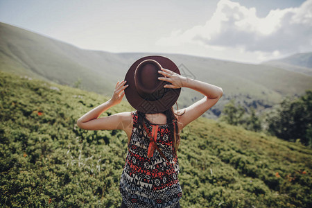 旅游癖和旅游概念时尚的旅行者女人戴着帽子看着山时髦女孩在山顶旅行图片