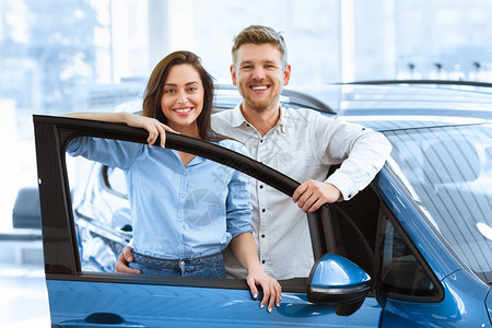 一对美丽幸福的夫妇在他们刚在经销商处买的一辆新车的敞开的门后合影图片