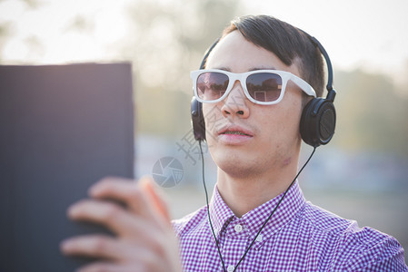 镇上的年轻青男子在太阳镜中用耳机和平板电脑监图片