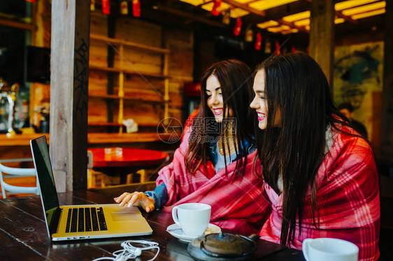 两个年轻漂亮的女孩坐在桌旁在网上找东西图片