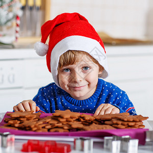 穿着红圣塔帽的可爱小男孩配着新鲜烤姜饼干祝大家对姜饼男人快乐背景图片