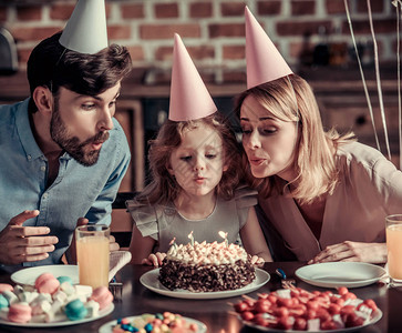 快乐的父母和女儿在生日庆祝活动期间坐在装饰厨房的桌子旁图片