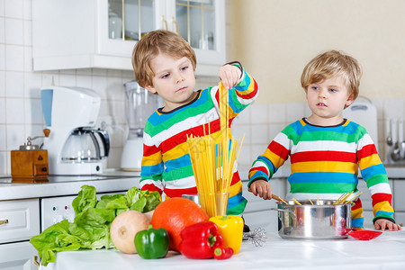 两个小男孩在厨房里用新鲜蔬菜做意大利面穿着多彩衬衫的缠身儿童图片