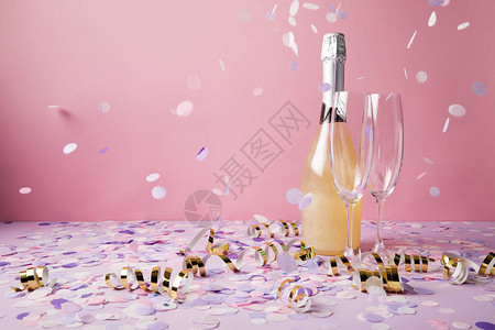 一瓶香槟玻璃杯和紫色表面上落下的五彩纸屑图片