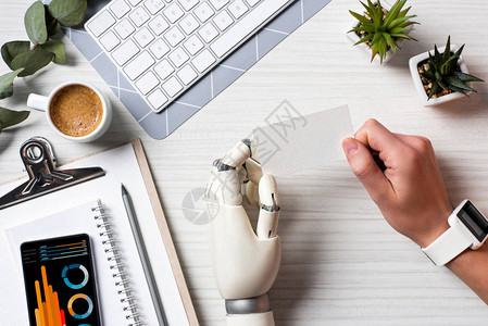 用机器人手和智能手表在桌子上拿着空白访问卡的商人的裁剪图像图片