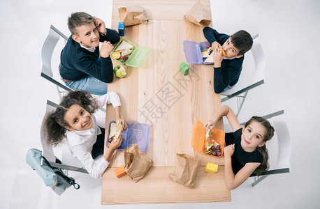 多族裔学生坐在桌边笑着看镜头时吃午餐的压倒视线图片