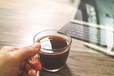 手握咖啡杯或茶叶和数字桌码头智能键盘木制桌上的钢笔图片
