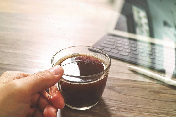 手握咖啡杯或茶叶和数字桌码头智能键盘木制桌上的钢笔图片