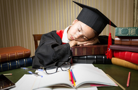 身着毕业帽子躺在满书的桌子上的沉睡女图片