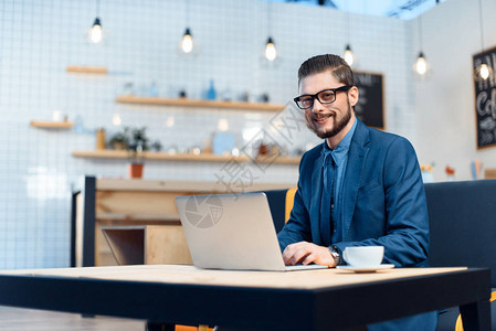 戴眼镜的英俊年轻商人使用笔记本电脑和在咖啡图片